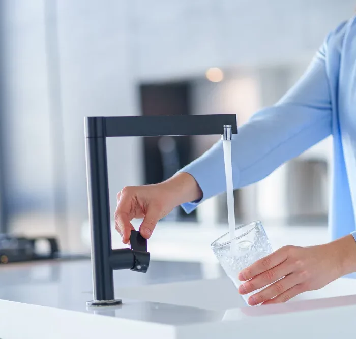 Personne remplissant un verre d'eau au robinet noir design dans une cuisine moderne.