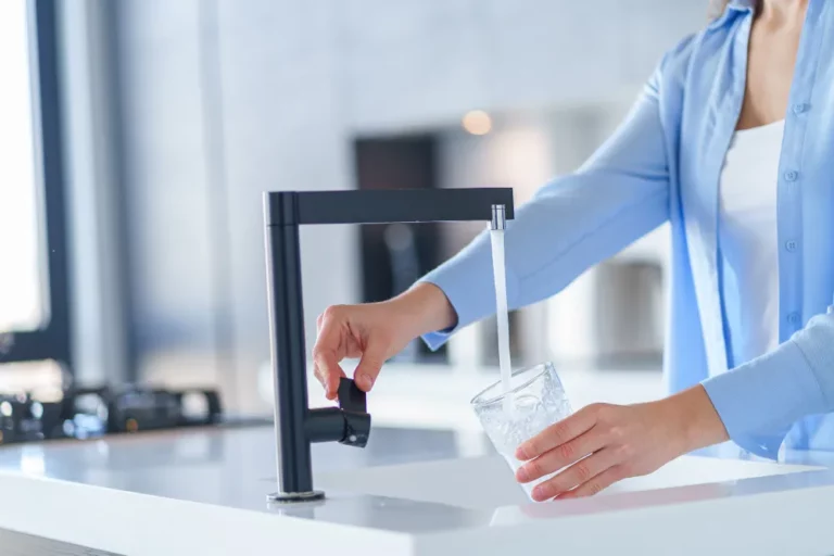 Personne remplissant un verre d'eau au robinet noir design dans une cuisine moderne.